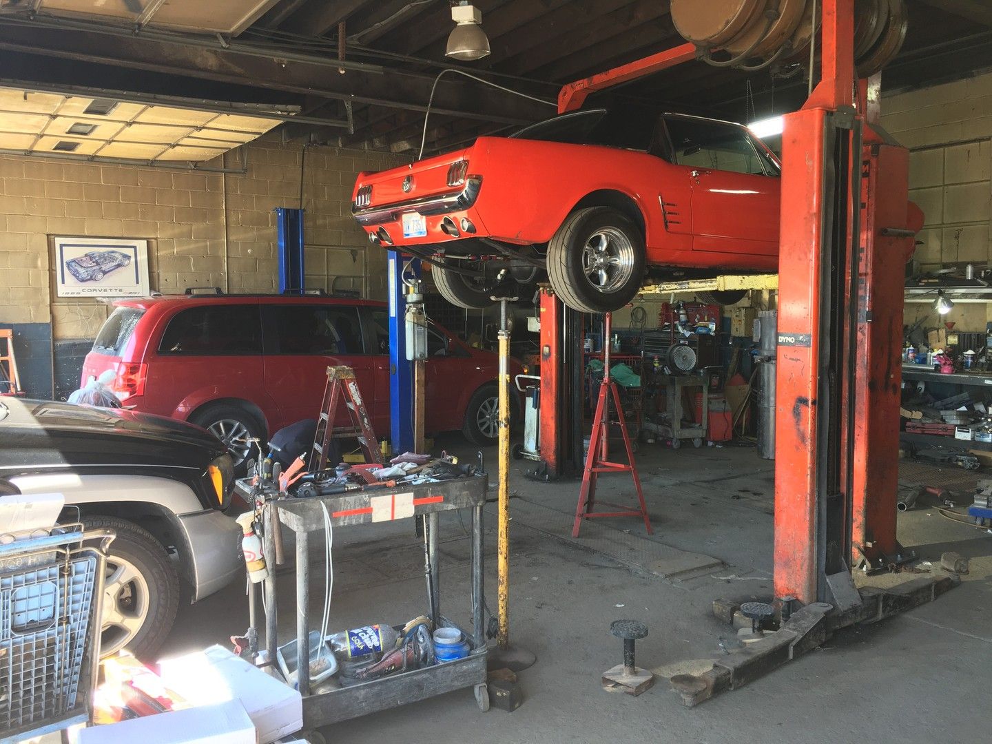 Inside the service bays: a classic red Ford Mustang raised on a lift, with a red minivan on a second lift